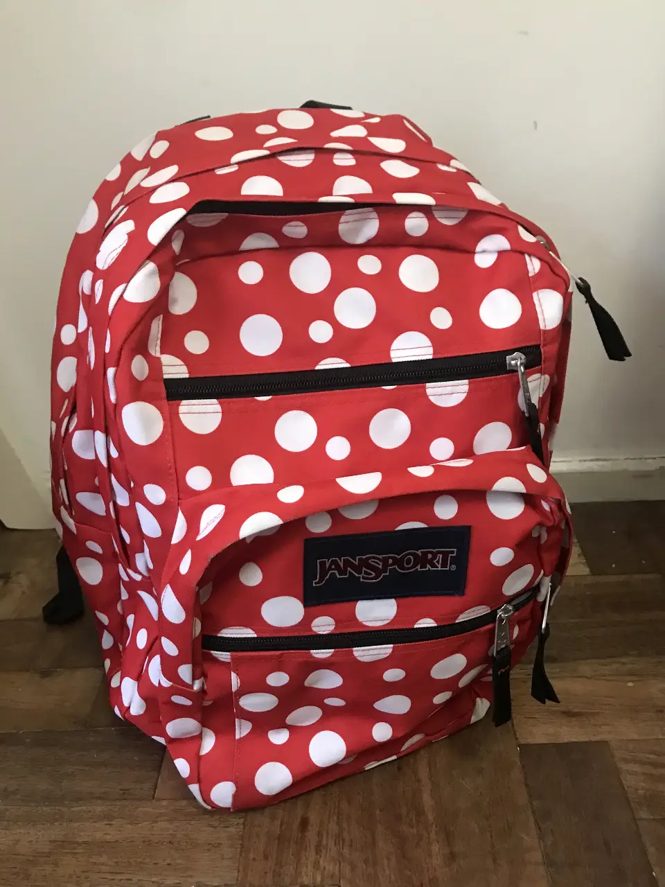 Mochila Jansport Big Student roja con lunares blancos. Ideal para llevar libros, útiles escolares o para uso diario. Cuenta con múltiples compartimentos y el logo de la marca.