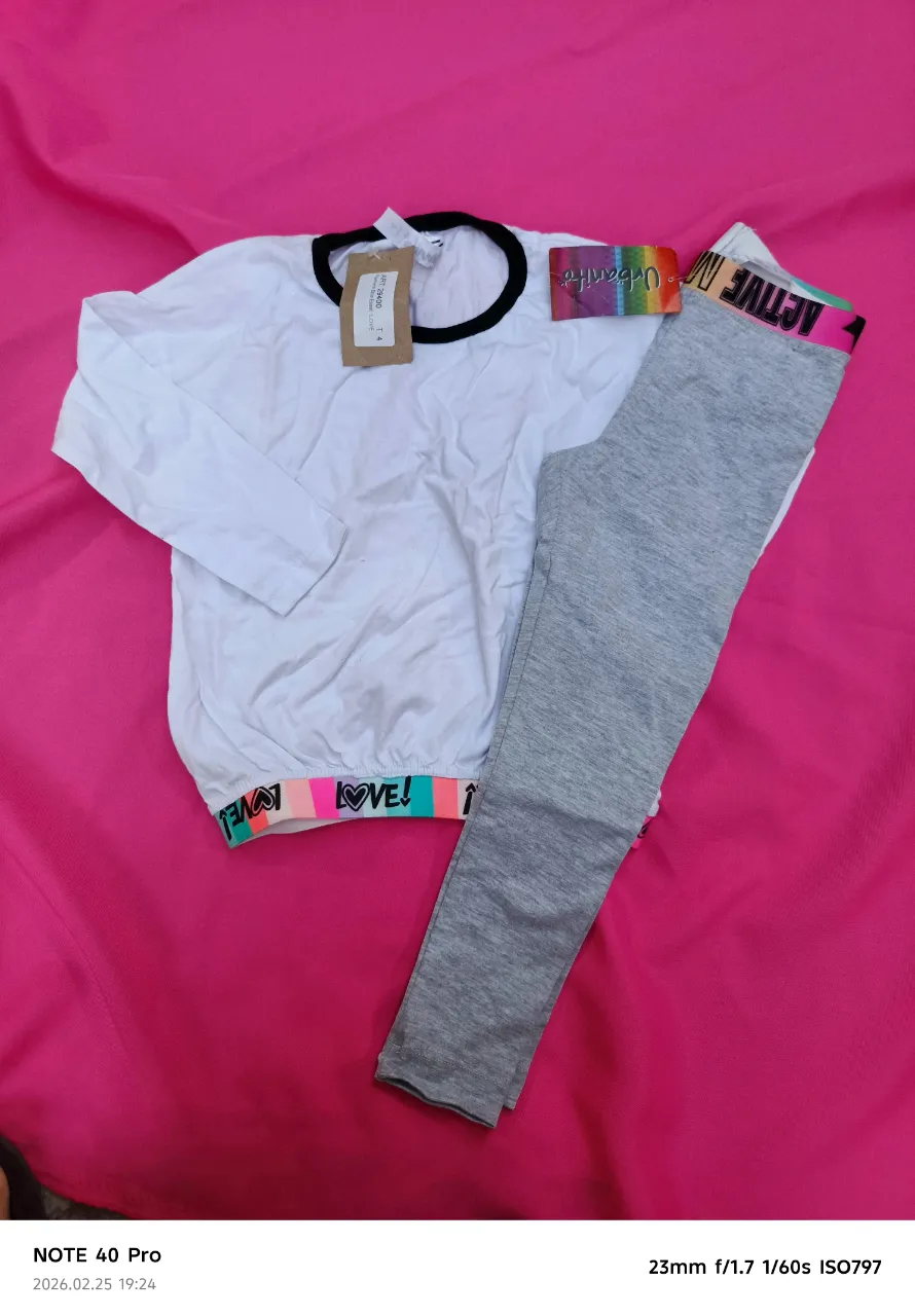 Conjunto deportivo de remera manga larga blanca con cuello y puños negros, y calzas grises. La cintura de las calzas tiene un elástico multicolor con la inscripción "ACTIVE" y corazones. Ideal para niñas activas y cómodas.