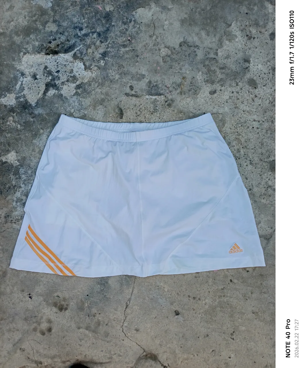 Shorts pollera deportivos blancos de Adidas con detalles de tres franjas naranjas en el lateral. Ideales para entrenar o para un look casual deportivo.