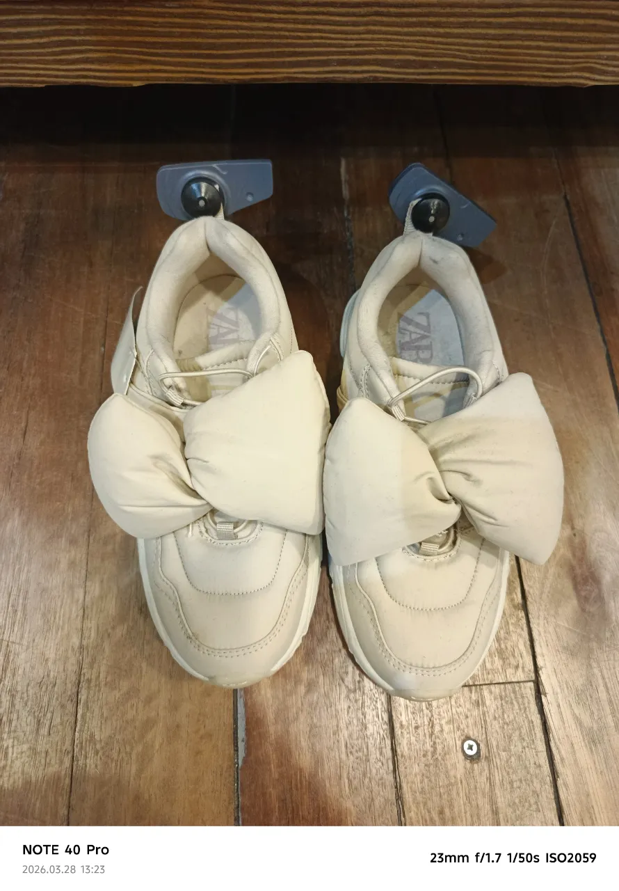 Zapatillas color beige con moño grande en la parte delantera. Suela blanca.