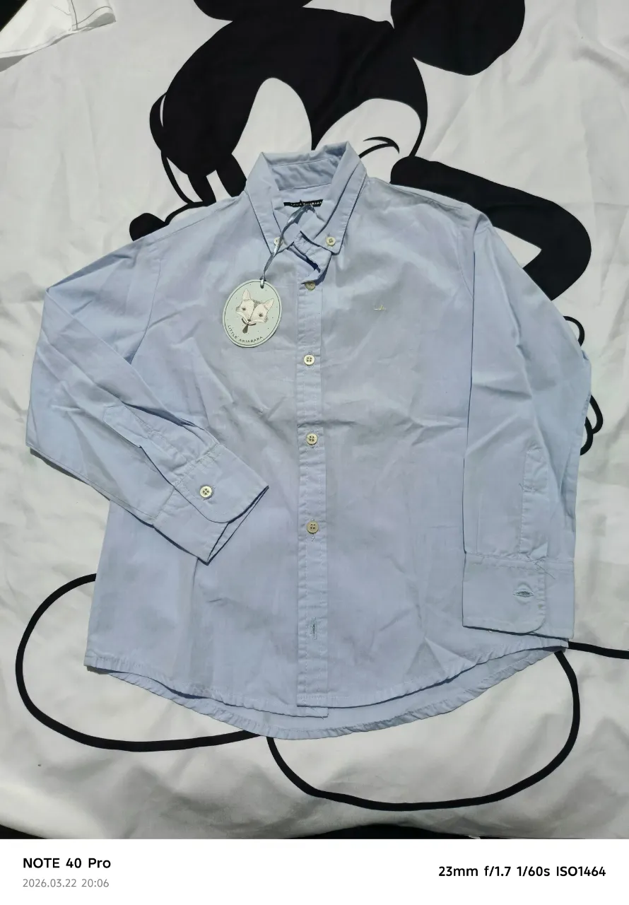 Camisa de manga larga de color celeste. Posee cuello con botones y puños abotonados. Tiene un pequeño bordado en el frente.