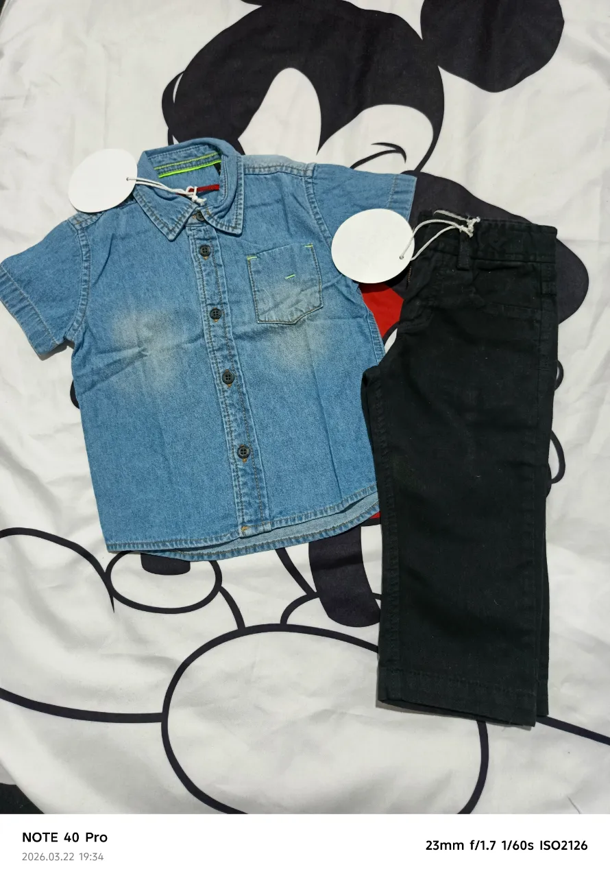 Camisa de jean de manga corta para niño. Posee cuello camisero, botones al frente y un bolsillo en el pecho con detalles de costura en color verde. La tela es de jean con un lavado desgastado.