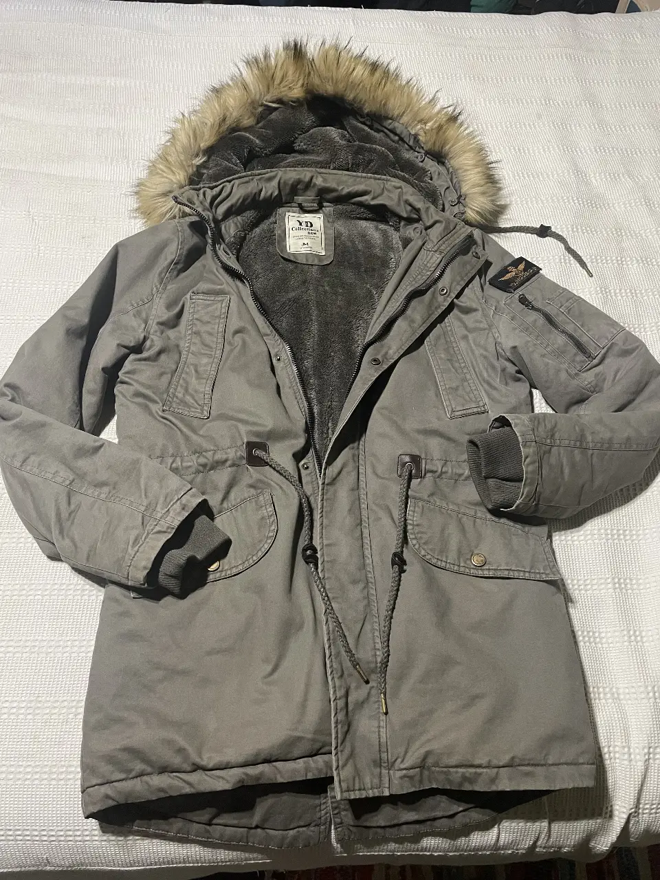 Campera de abrigo para hombre, color gris, con capucha con borde de piel sintética, cierre y bolsillos.