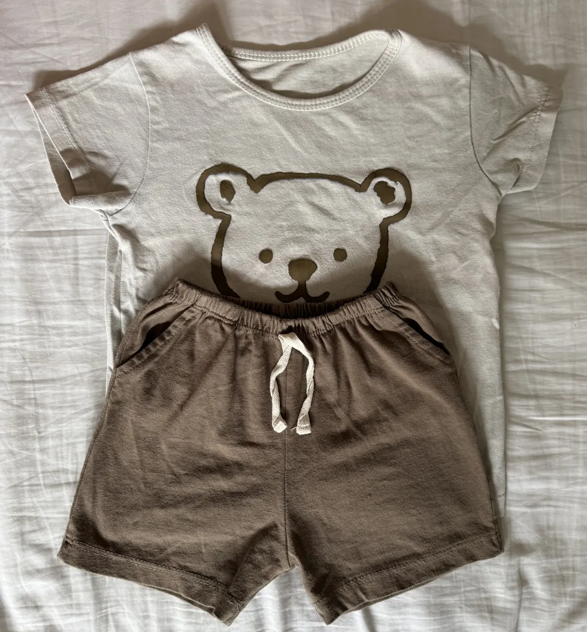 Conjunto de remera y short de algodón para bebé. La remera es de color crudo con un estampado de oso y el short es de color marrón.