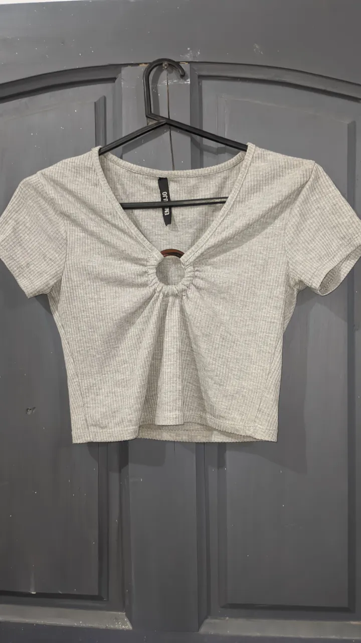 Remera gris de manga corta con escote en V y detalle de aro metálico en el centro.