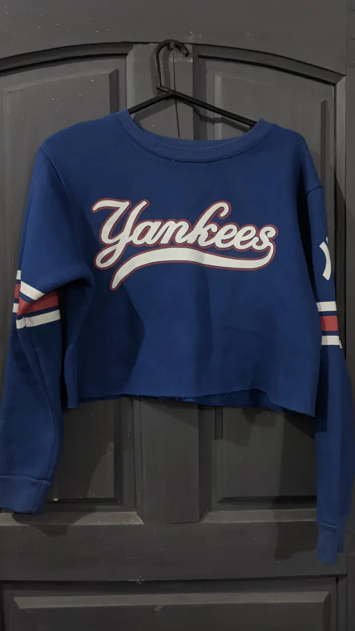 Buzo cropped azul con logo de "Yankees" en blanco y rojo. 
