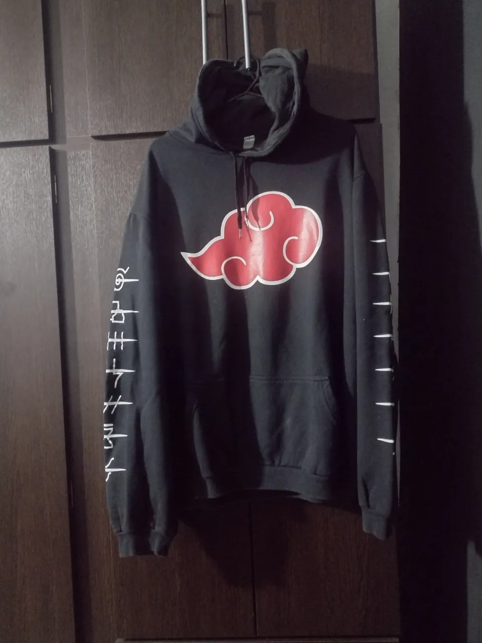 Buzo negro con capucha, estampado de nubes rojas y símbolos en las mangas. Ideal para fans de anime y estilo urbano.