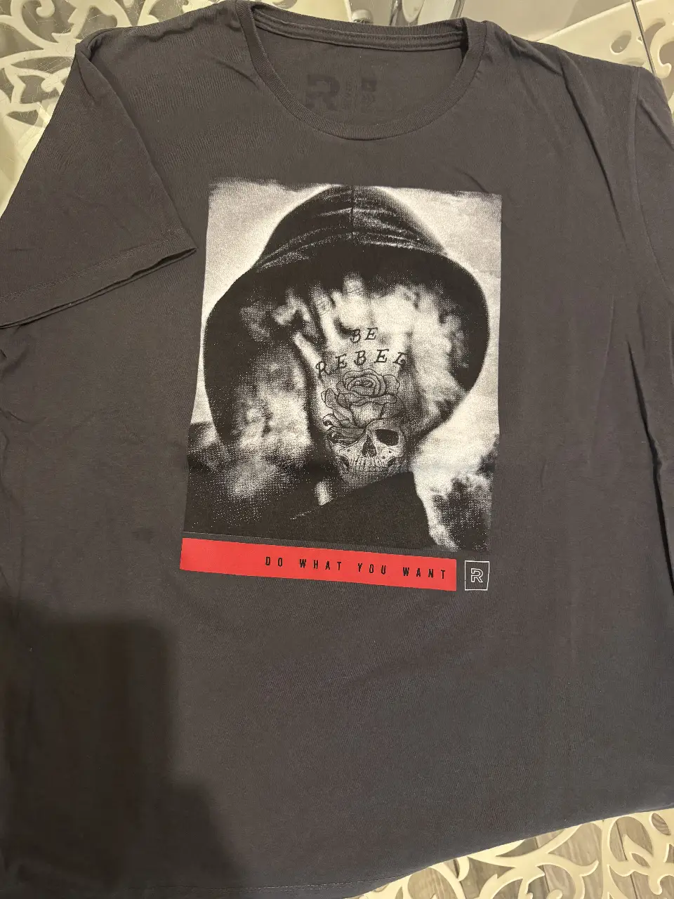 Remera de hombre gris con estampado frontal de diseño "Be Rebel" con imagen de rostro y frase "Do what you want". Ideal para un look urbano y rebelde.