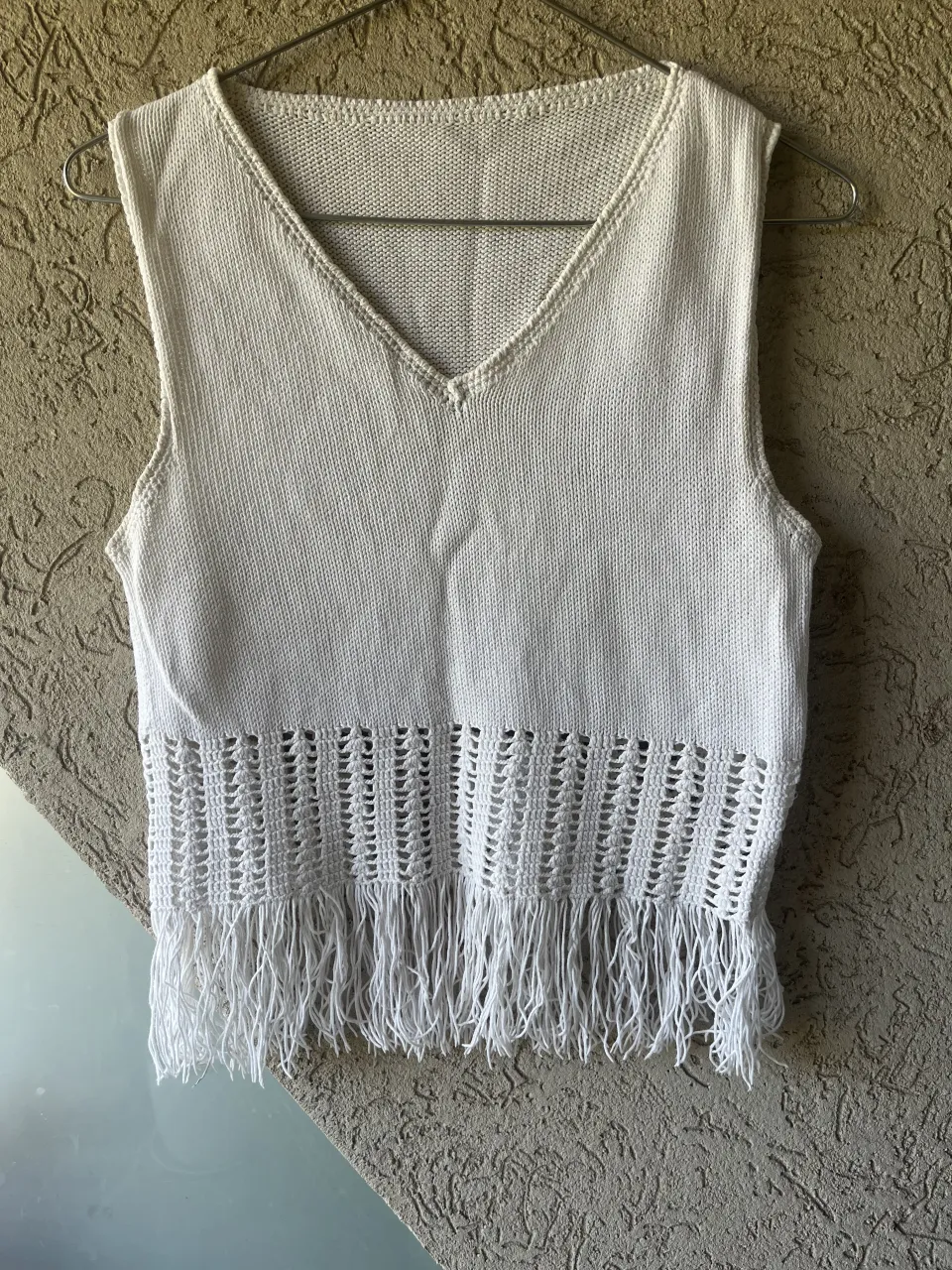Musculosa tejida color blanco con escote en V y detalles de macramé y flecos en la parte inferior.