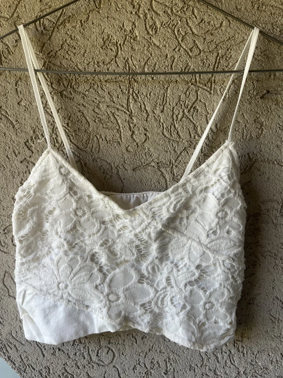 Top blanco de breteles finos con detalles de encaje floral en toda la prenda. El bajo es liso y de algodón.