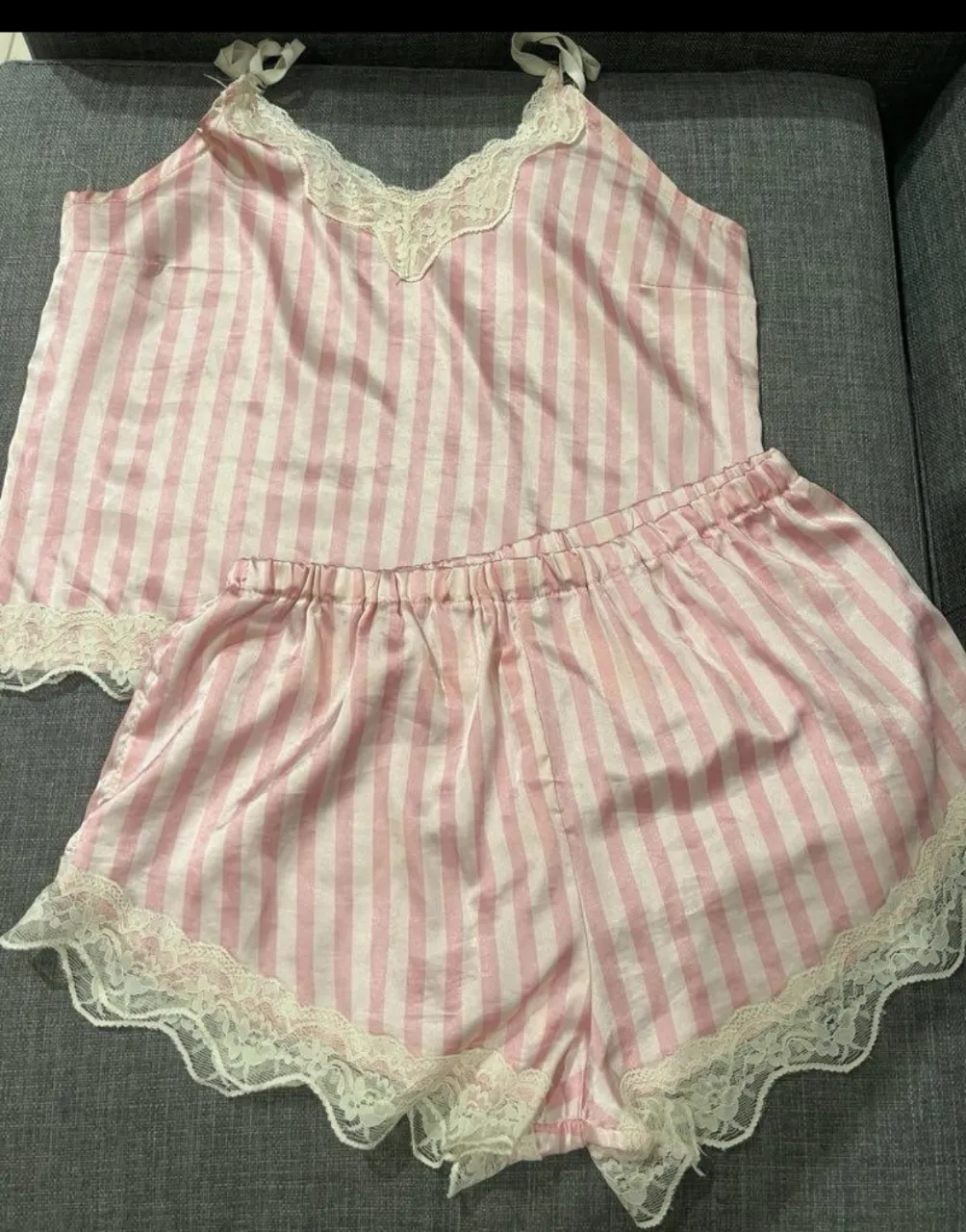 Conjunto de pijama de dos piezas a rayas rosas y blancas. Incluye una musculosa con breteles finos y detalles de encaje en el escote y ruedo. El short tiene cintura elastizada y también detalles de encaje en el ruedo.