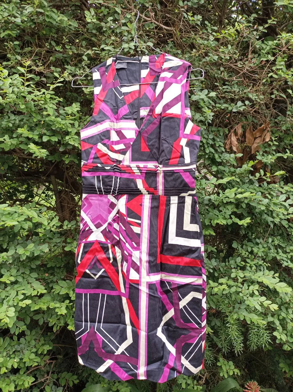 Vestido de fiesta con estampado geométrico vibrante en colores negro, fucsia, rojo y blanco. Diseño sin mangas con escote en V y detalles fruncidos en la cintura que estilizan la figura. Ideal para eventos y ocasiones especiales.