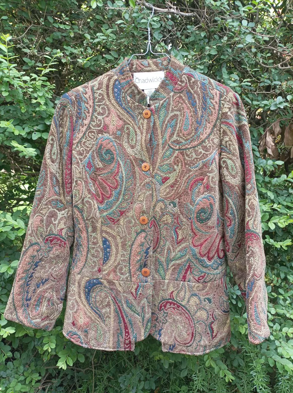 Chaqueta tipo blazer con un estampado paisley vibrante en tonos tierra, azul y rojo. Posee cuello mao, mangas largas y cierre de botones de madera. Ideal para un look elegante y con un toque bohemio.