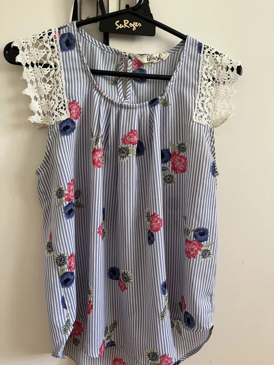 Remera a rayas celestes y blancas con estampa floral de flores rojas y azules. Posee detalles de encaje blanco en las mangas y un corte en la espalda.