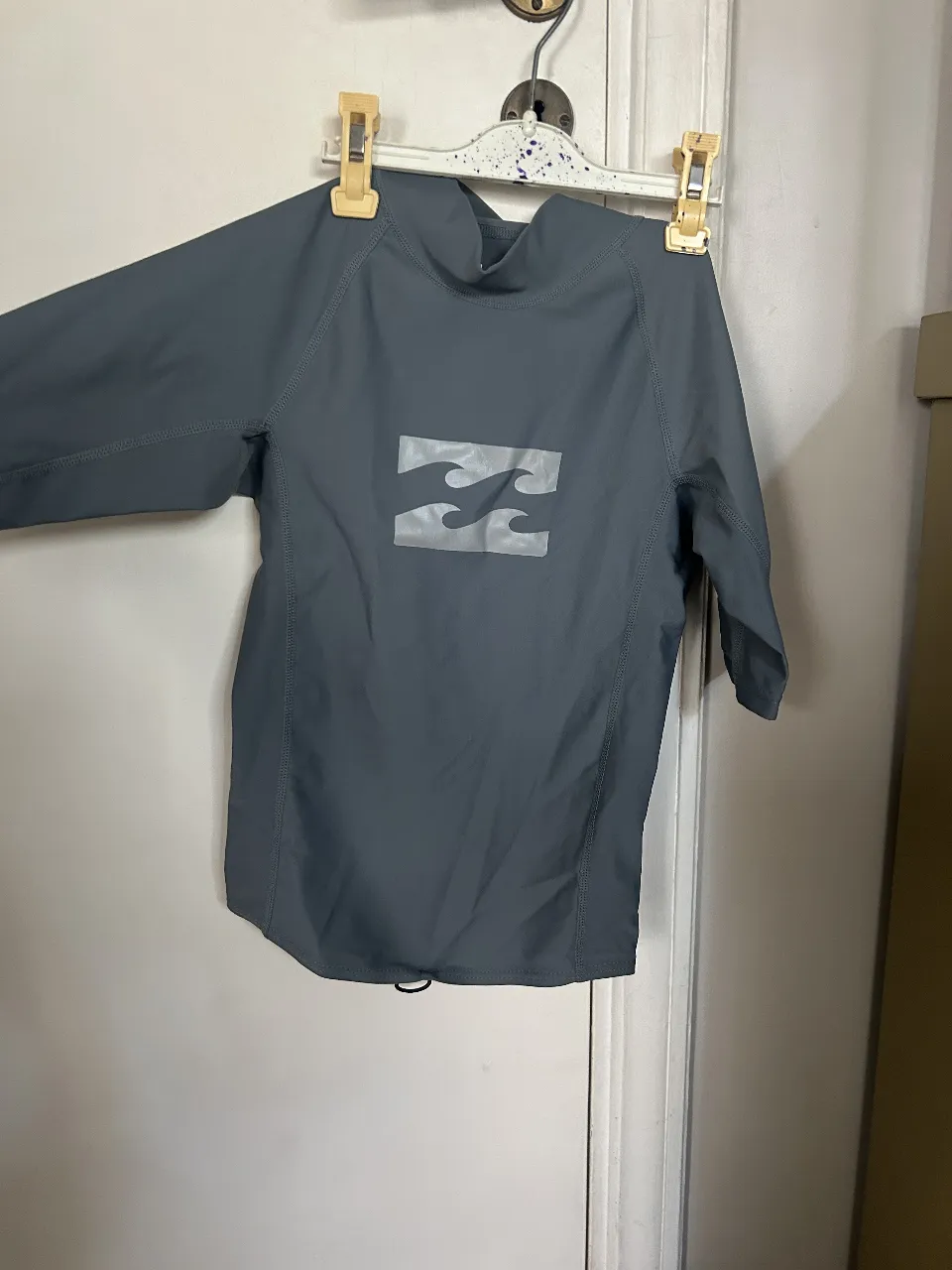 Remera deportiva manga larga Billabong, color gris, con logo estampado. Cuello alto y ajuste en la cintura. Ideal para actividades acuáticas.