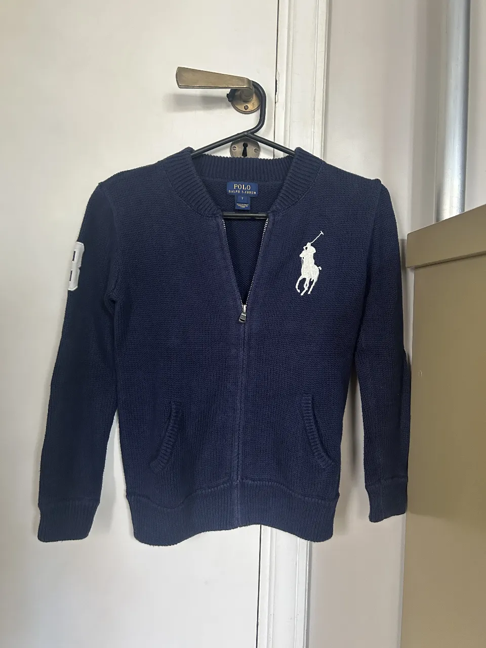 Buzo con cierre de la marca Polo Ralph Lauren, color azul marino, con el logo del jugador de polo bordado en blanco. Talle 7.