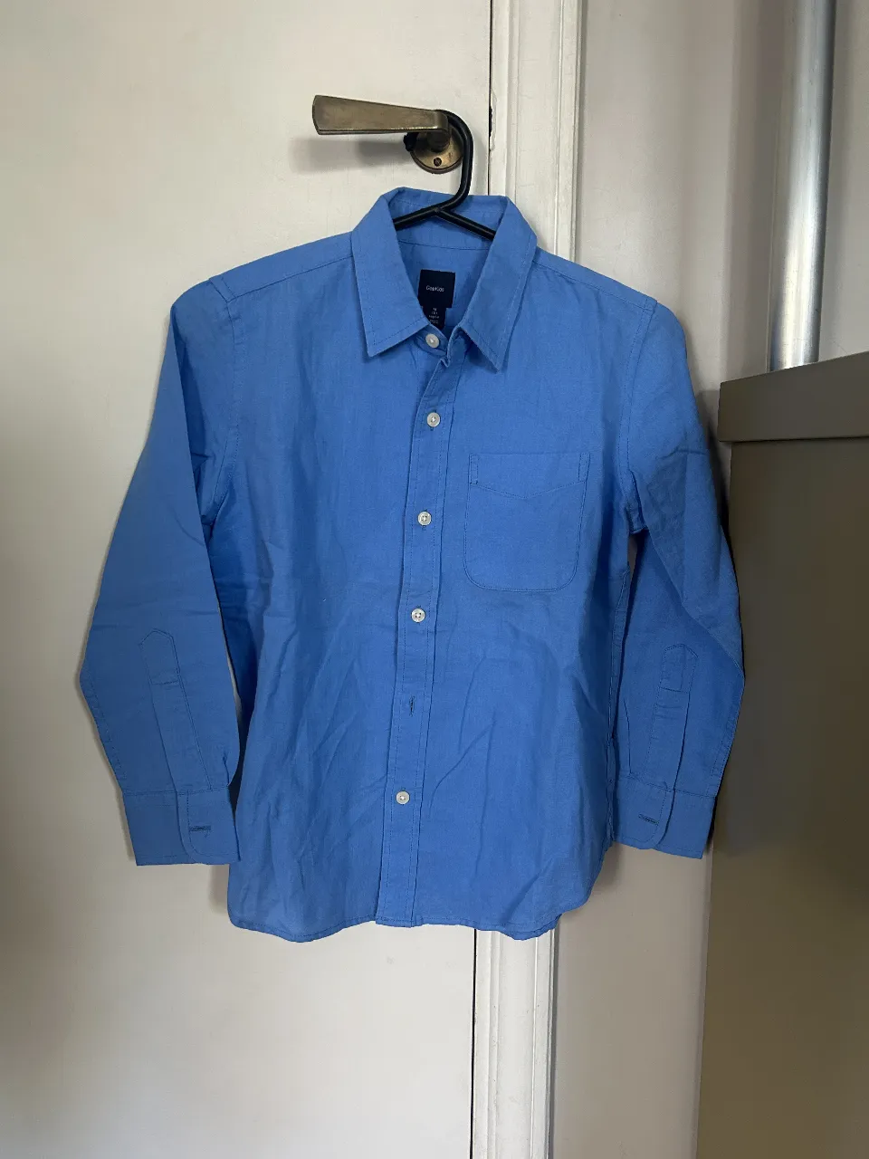 Camisa celeste de manga larga para niño, de la marca GapKids. Con un bolsillo en el pecho y botones blancos. Ideal para un look casual y cómodo.