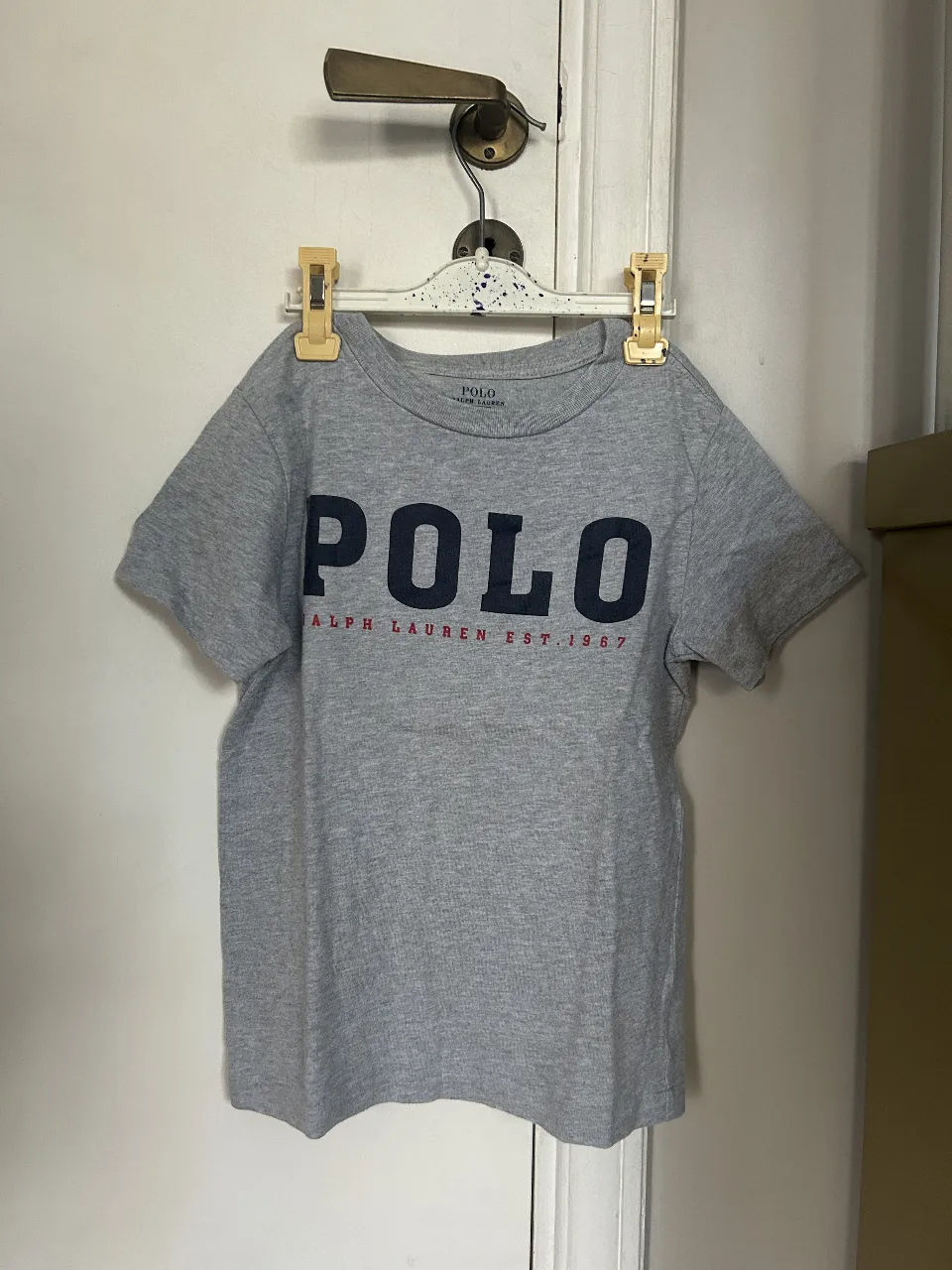 Remera de niño Polo Ralph Lauren, gris con el logo "POLO" en azul marino y la inscripción "RALPH LAUREN EST. 1967" en rojo. Ideal para un look casual y cómodo.