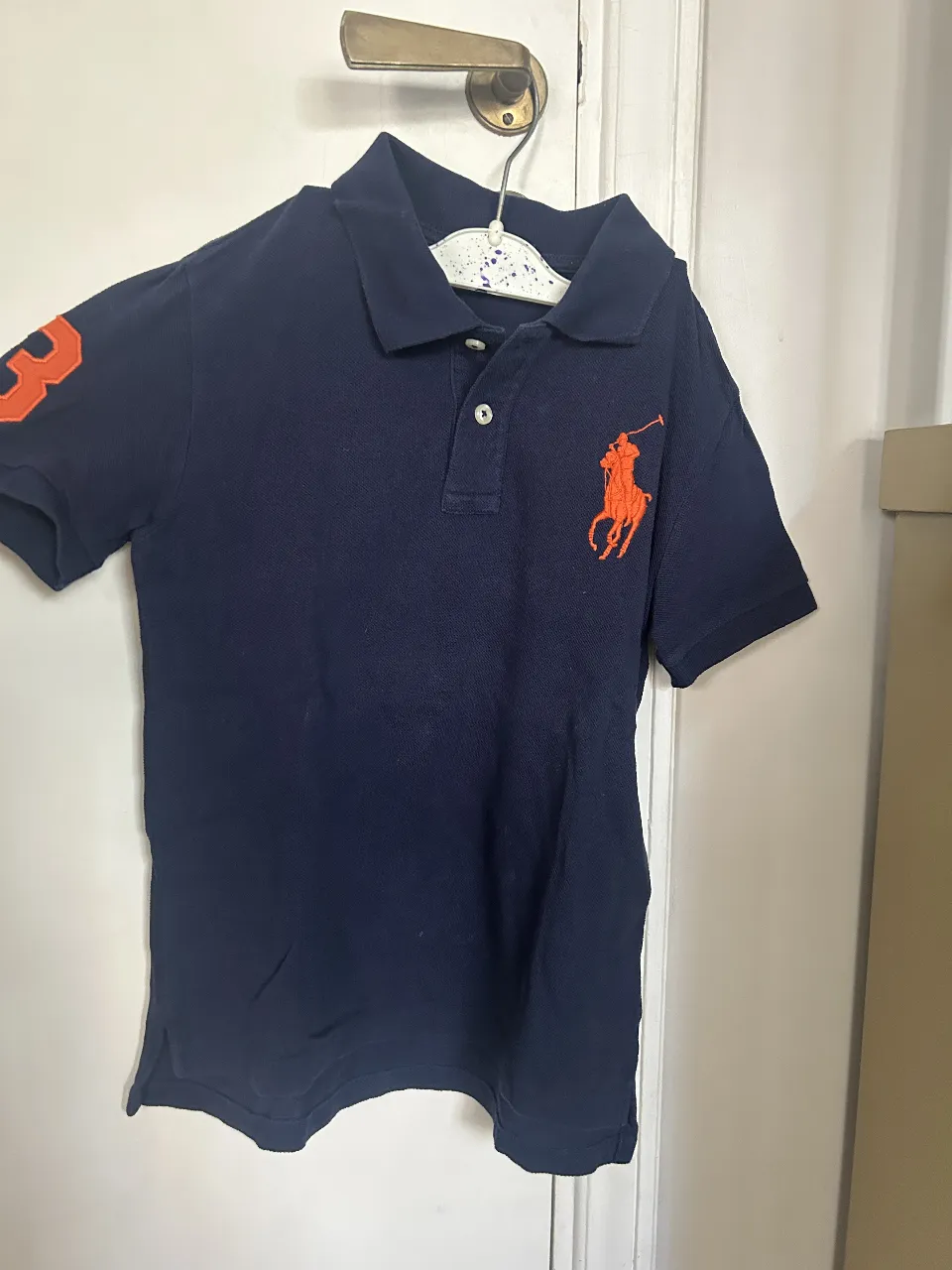 Remera polo de niño, azul marino con el logo de Ralph Lauren en naranja. Talle 7.