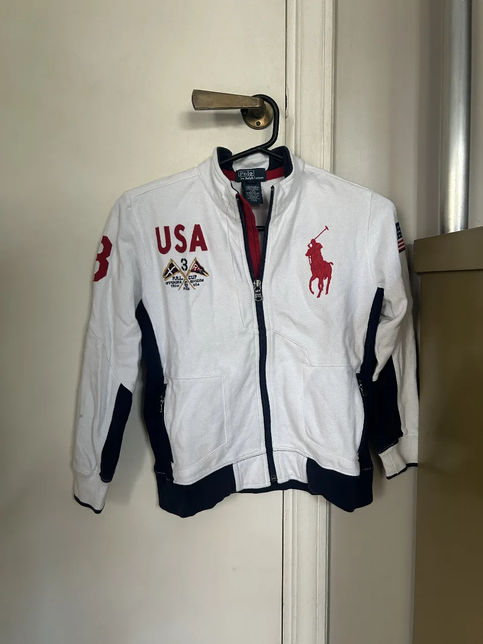 Campera deportiva de niño, con cierre y detalles en azul marino. Diseño con el logo de Polo by Ralph Lauren y detalles de USA. Talle 6.