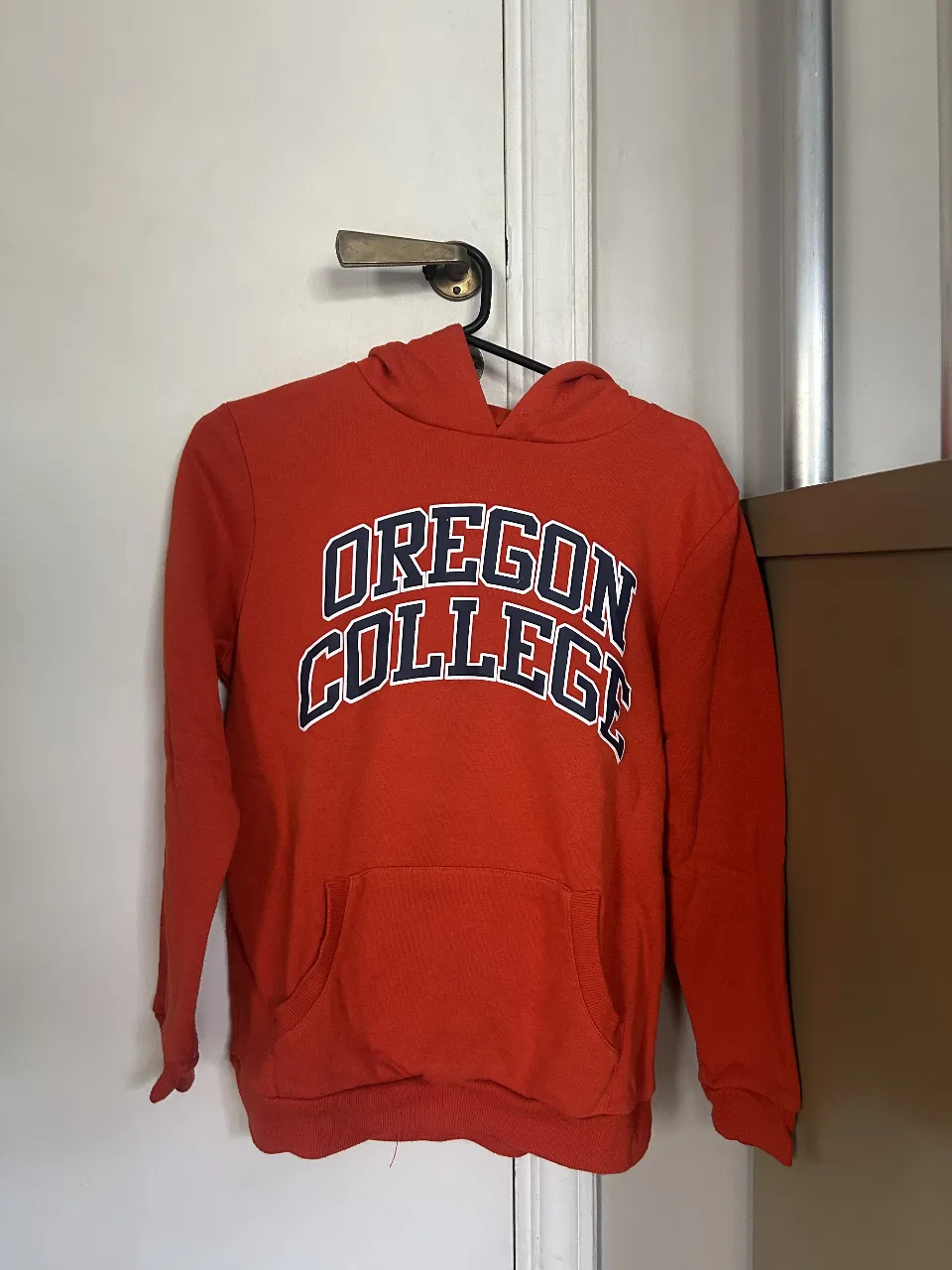 Buzo canguro rojo de la marca Primark, con estampado "OREGON COLLEGE" en la parte delantera. Ideal para un look casual y cómodo.
