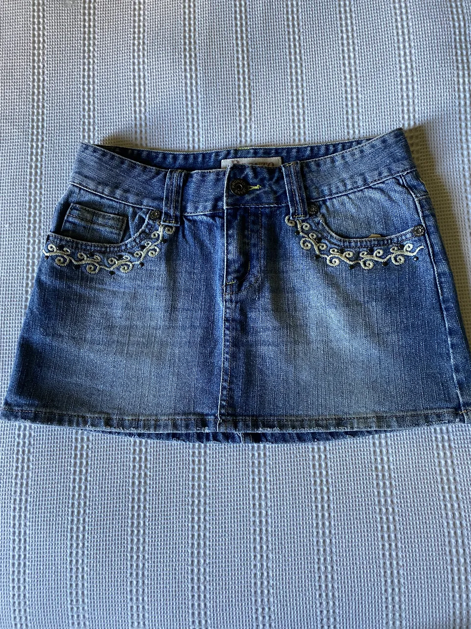 Minifalda de jean azul con detalles bordados en los bolsillos delanteros y traseros. Ideal para un look casual y juvenil.