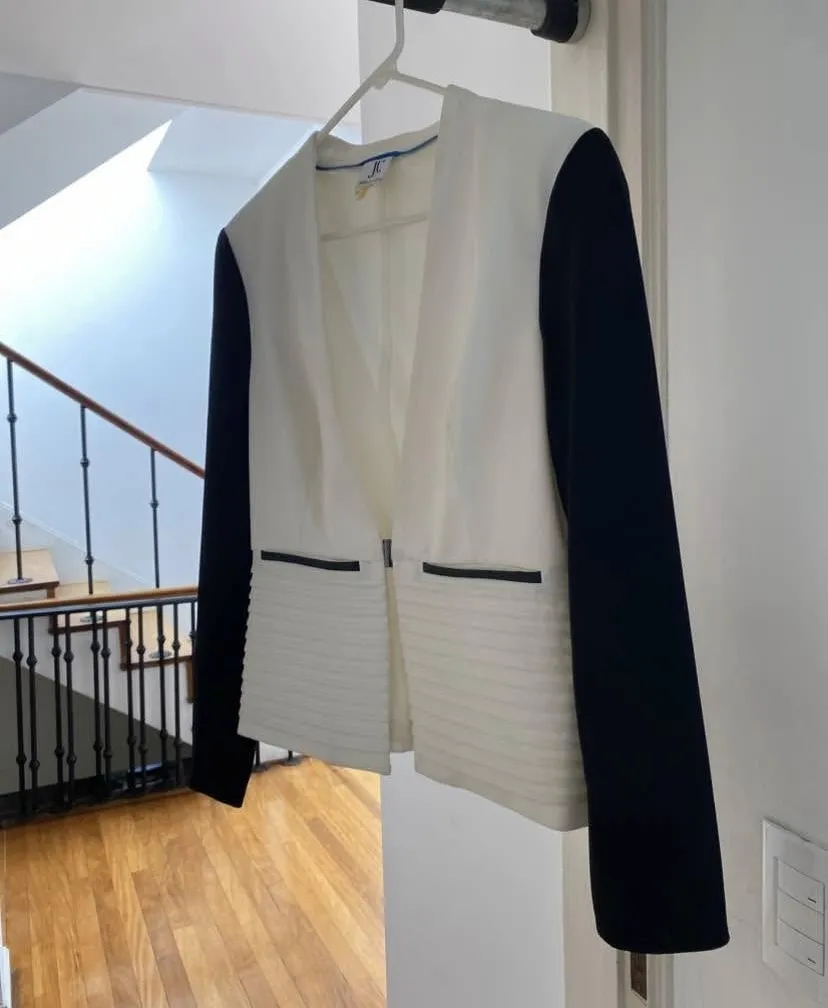 Blazer de mujer en color blanco con mangas negras. Diseño con solapas y detalle de costuras horizontales en la parte inferior. Ideal para un look elegante y moderno.