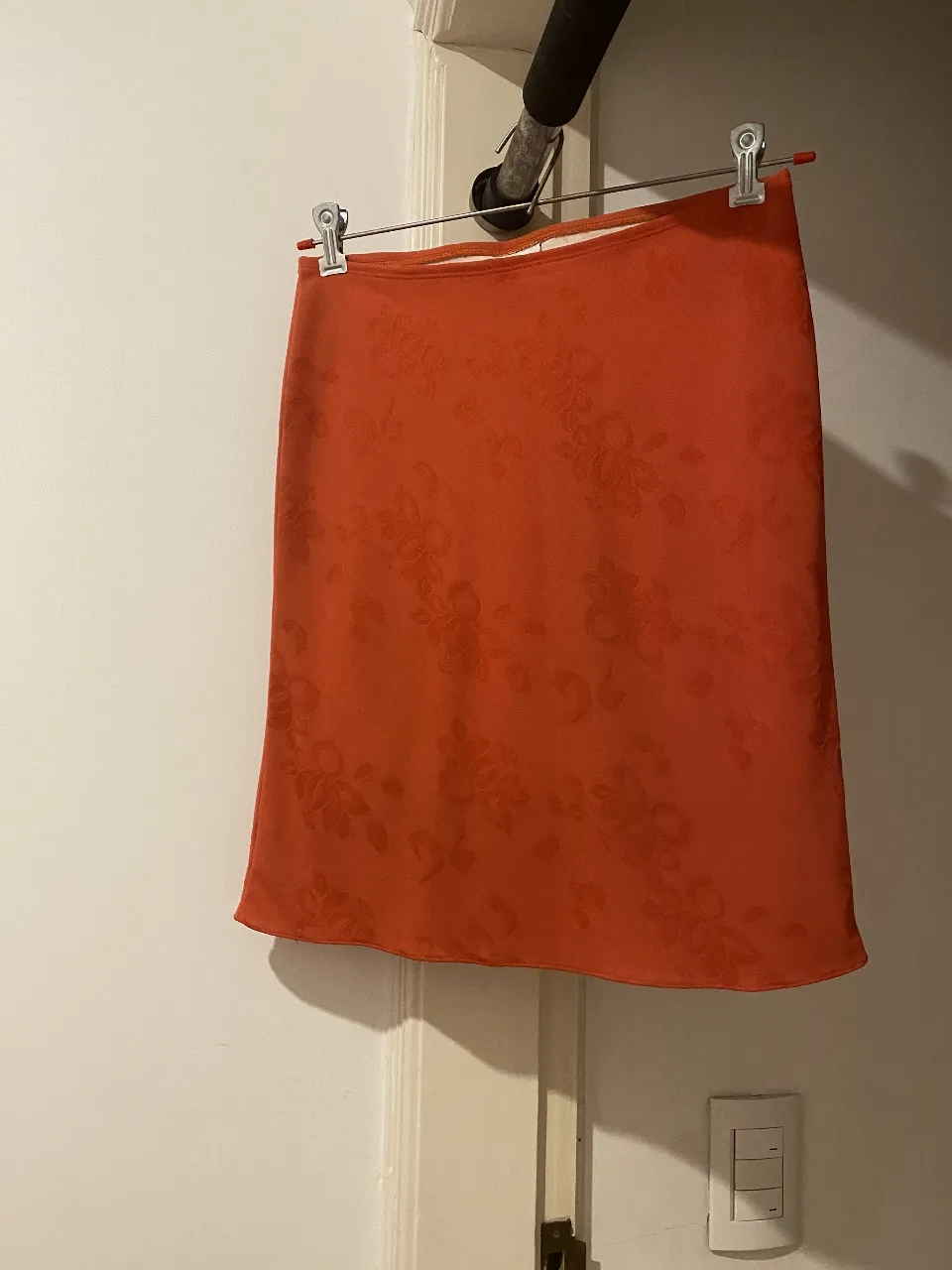 Pollera sobre rodilla, forrada,  color coral, con estampado floral en relieve. Ideal para un look vintage y elegante.