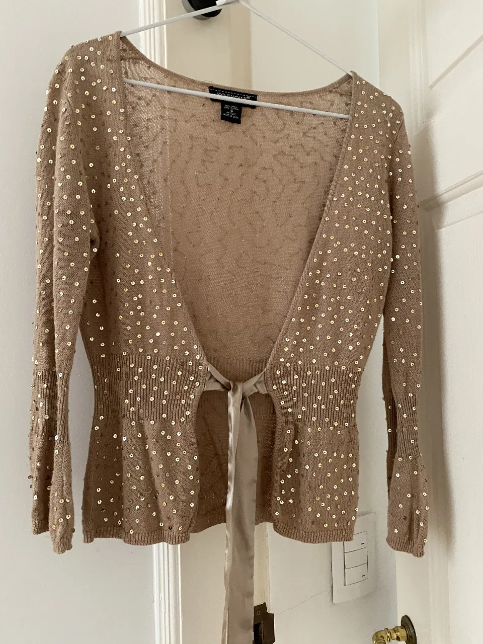 Cardigan de mujer color beige con lentejuelas doradas. Ideal para fiestas o eventos especiales. Con lazo para ajustar en la cintura.