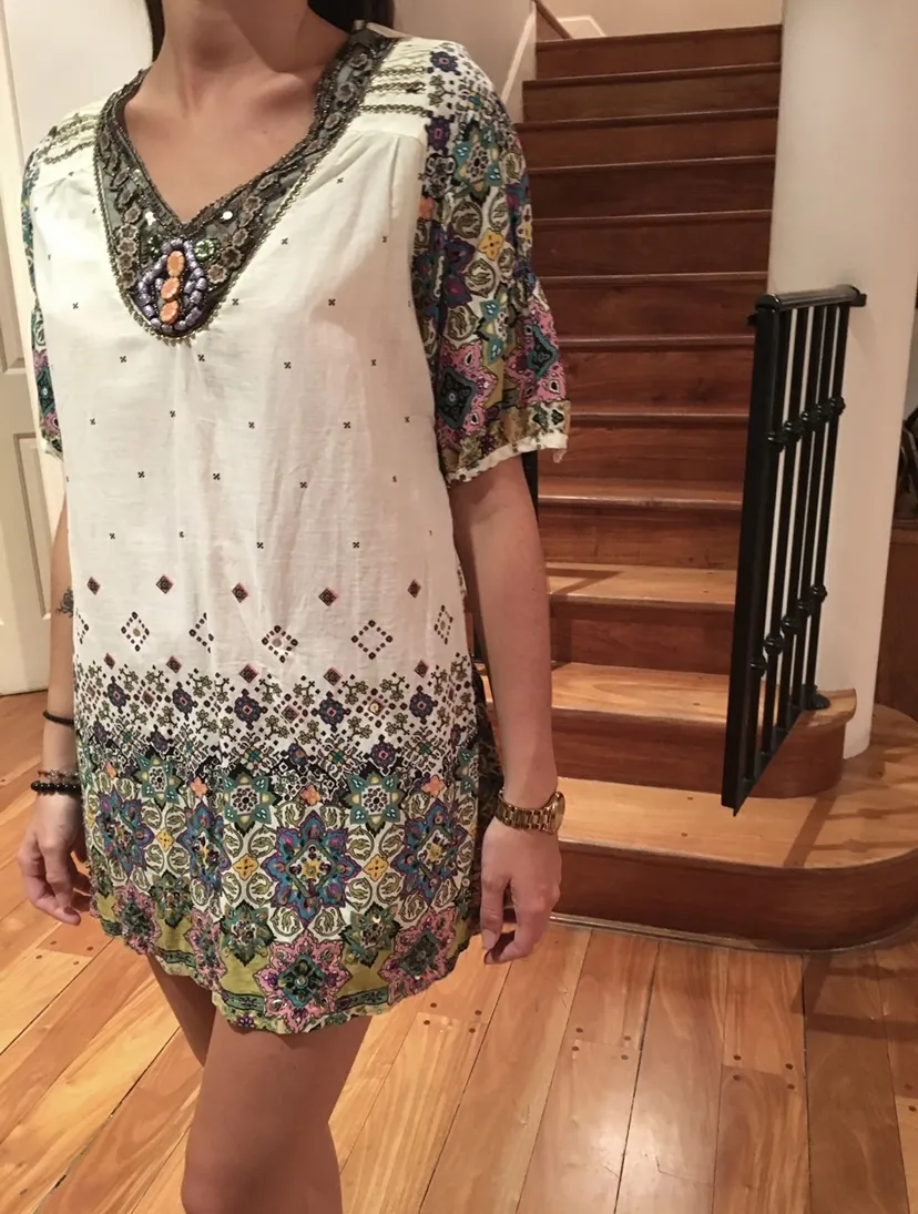 Blusa española color natural con mangas cortas y escote en V. Posee un estampado étnico y floral en la parte inferior y en las mangas. El escote y el ruedo tiene bordados con piedras, mostacillas y lentejuelas. Ideal para un look boho chic.