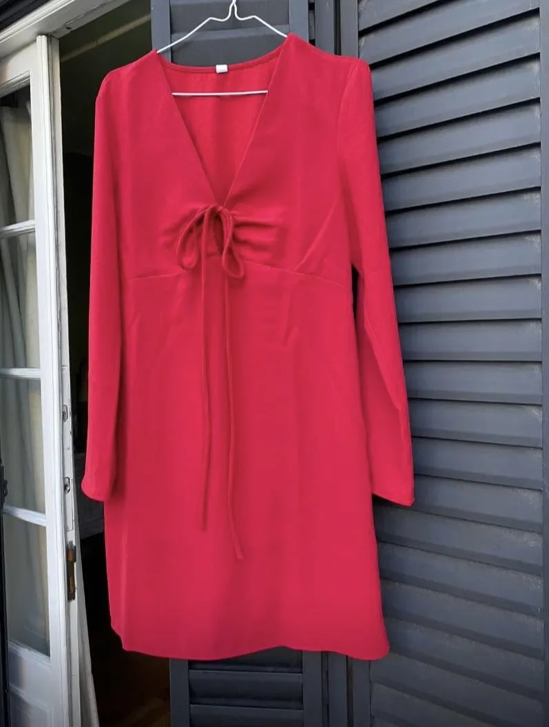 Vestido corto sobre rodilla, rojo, con escote en V y detalle de lazo en el pecho. Manga larga. Ideal para una salida o fiesta.
