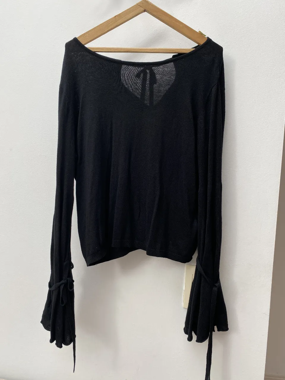 Sweater negro de manga larga con detalle de lazo en la espalda y mangas acampanadas. Ideal para un look elegante y sofisticado.