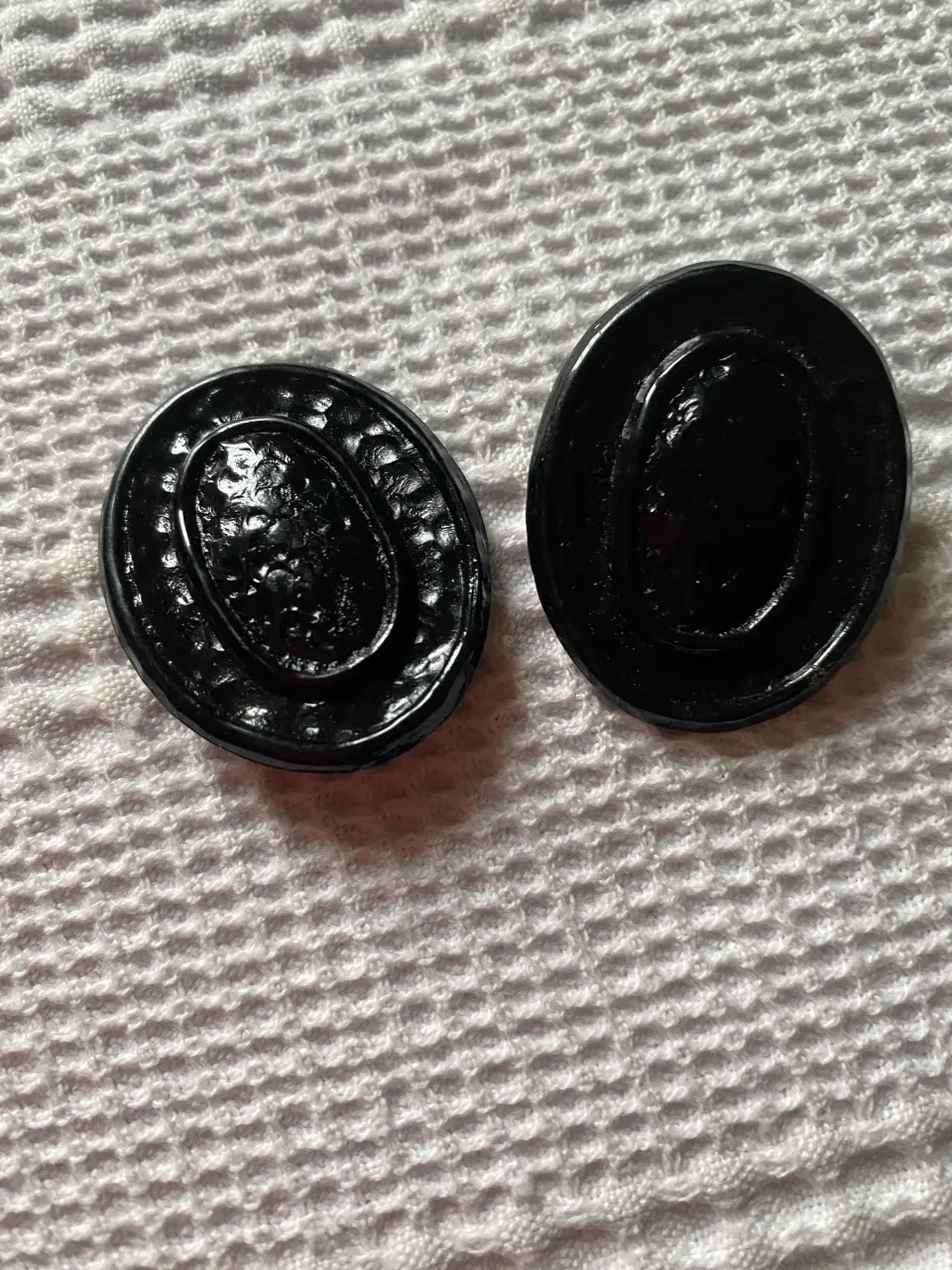 Par de aros negros, con diseño ovalado y detalles texturizados en relieve. Cierre de clip, ideales para complementar cualquier look.