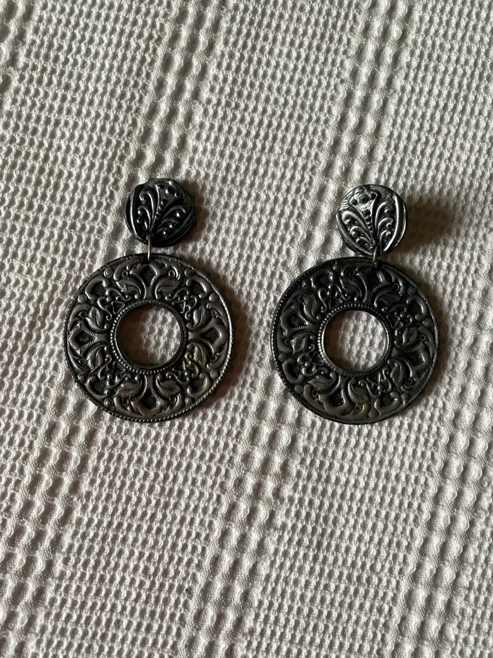 Aros colgantes plateados con diseño labrado y detalles calados. Un accesorio llamativo y elegante para realzar cualquier look.