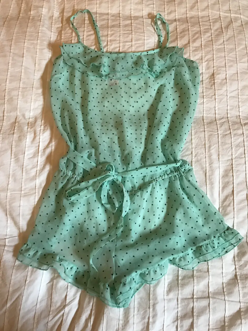 Mono corto de tela ligera y fresca, color verde agua,  ideal para el verano. Diseño con lunares, volados en el escote y en los bordes de las piernas. Incluye cinturón para ajustar la cintura.