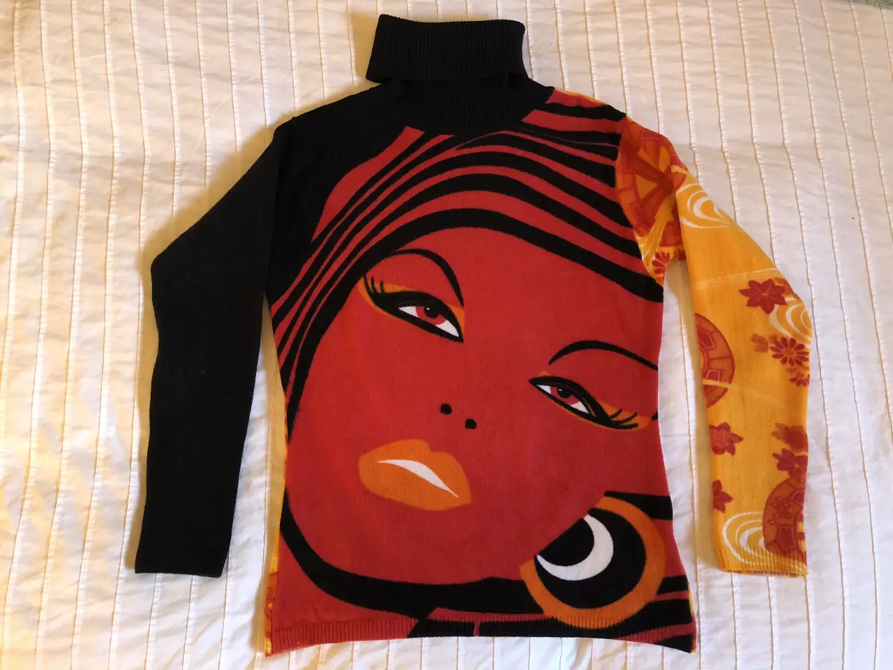 Sweater de cuello alto con diseño artístico de rostro femenino en tonos rojo y negro, manga larga negra y detalles en amarillo y naranja. Ideal para un look retro y llamativo.