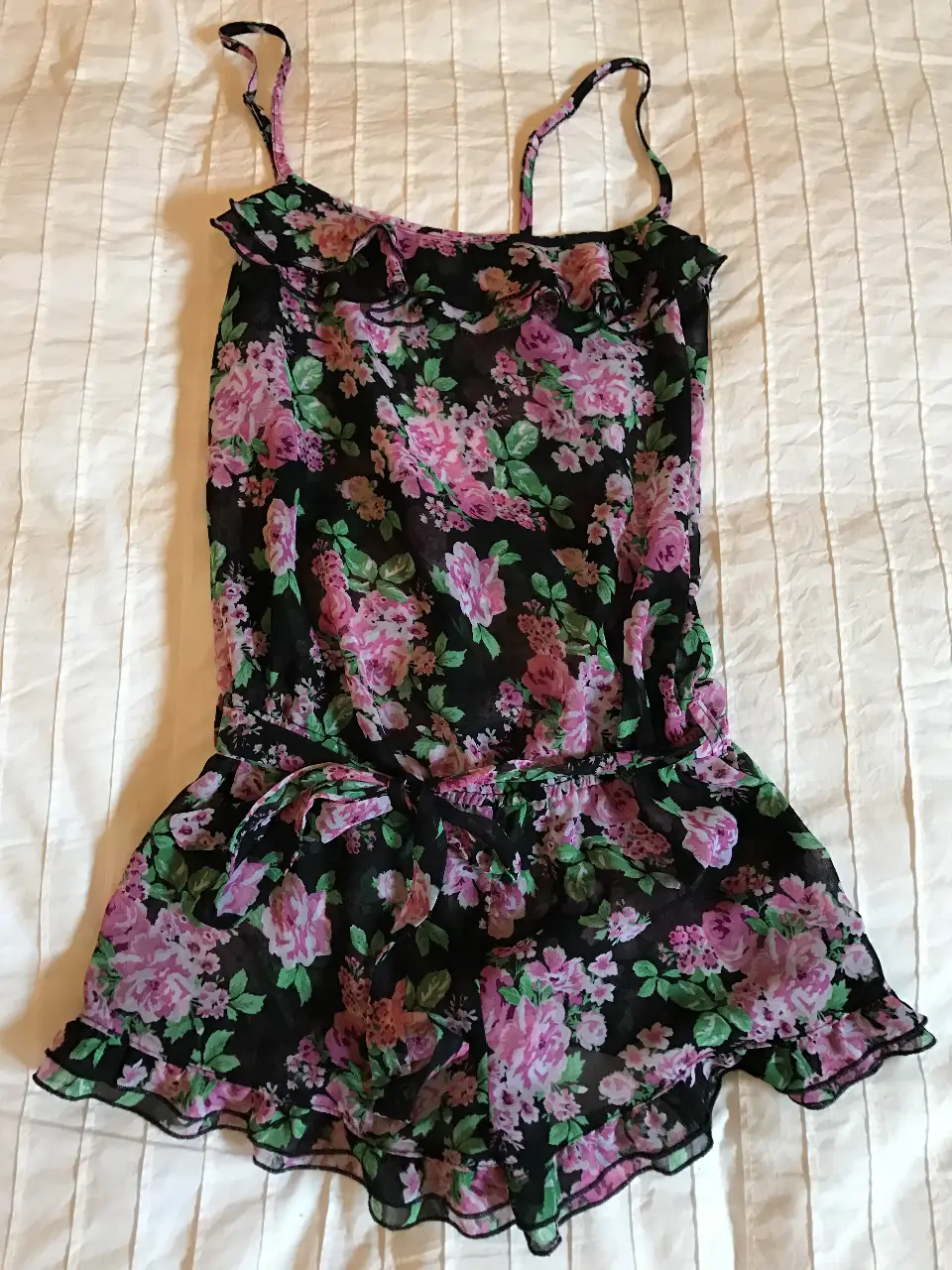 Mono de gasa con estampado floral en tonos rosa y negro. Diseño con tirantes finos, volados en el escote y en el borde inferior, y un lazo en la cintura para ajustar. Ideal para un look fresco y femenino.
