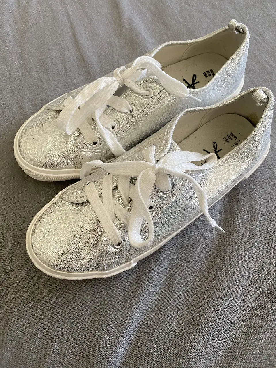 Zapatillas plateadas con cordones blancos, ideales para un look casual y moderno. Perfectas para combinar con cualquier outfit.