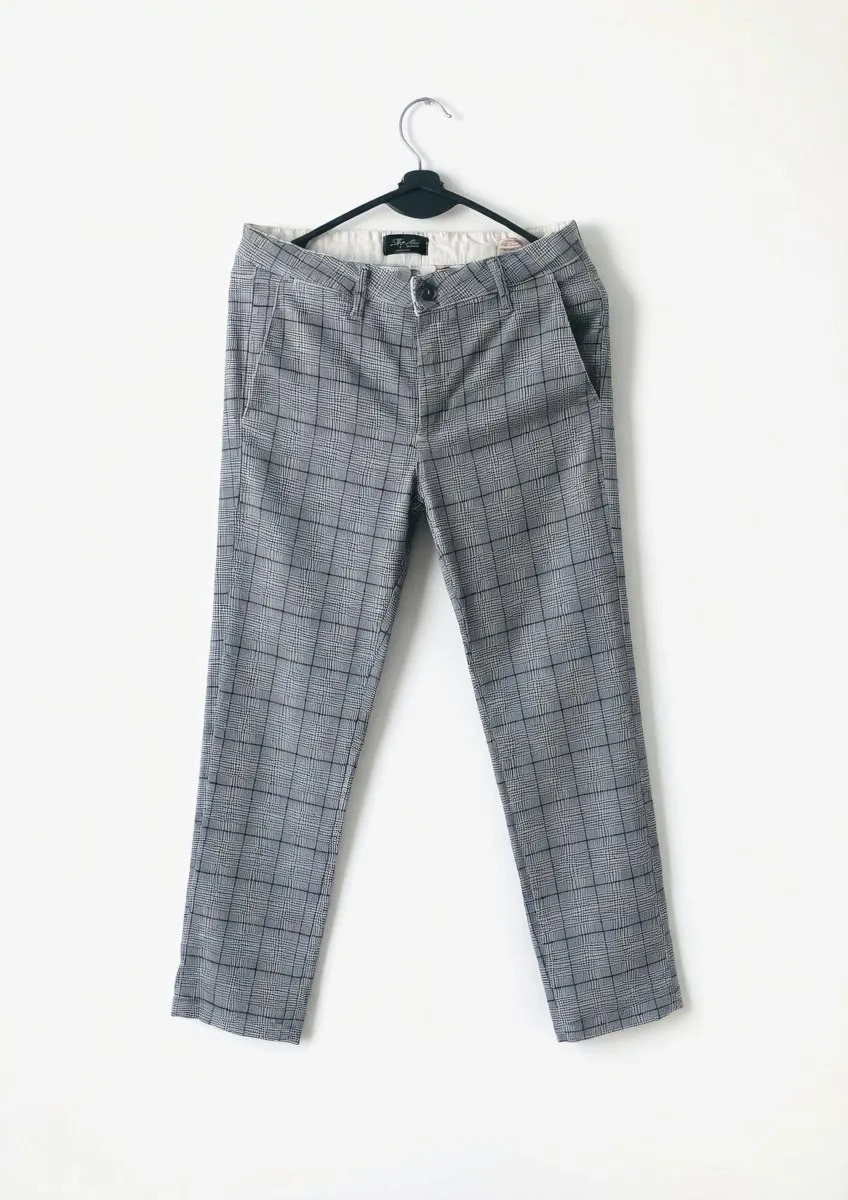 Pantalón de vestir a cuadros grises y blancos con detalles en azul. Posee bolsillos delanteros y traseros.