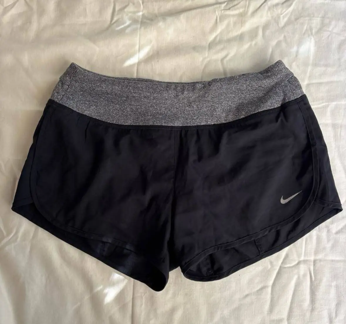 Short deportivo Nike para mujer, negro con cintura gris. Ideal para running y entrenamientos. Cuenta con bolsillo trasero con cierre y logo de la marca. talle S