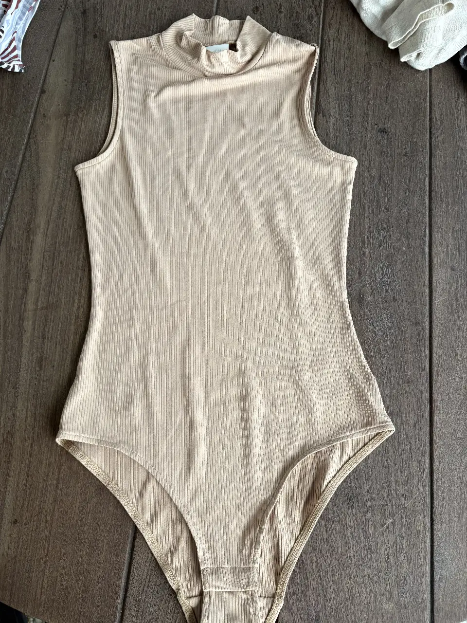 Body de mujer, color crudo, con cuello alto y sin mangas. Diseño liso con textura acanalada. Cierre inferior con broches.