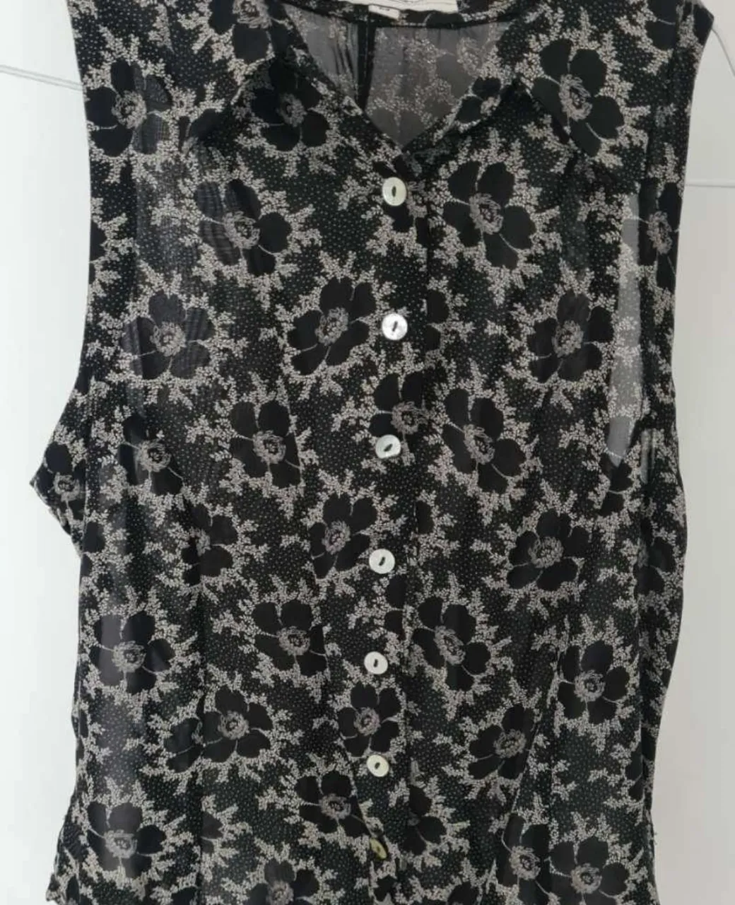 Blusa sin mangas con estampa floral en blanco y negro. Posee botones al frente y cuello camisero. Ideal para un look casual y fresco.