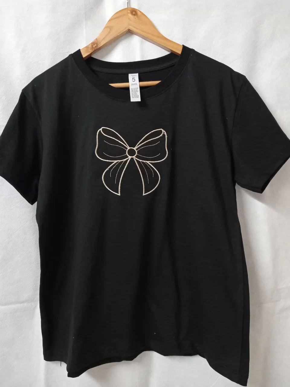 Remera negra con un bordado de moño en la parte delantera. Diseño delicado y original, ideal para darle un toque chic a tu outfit.