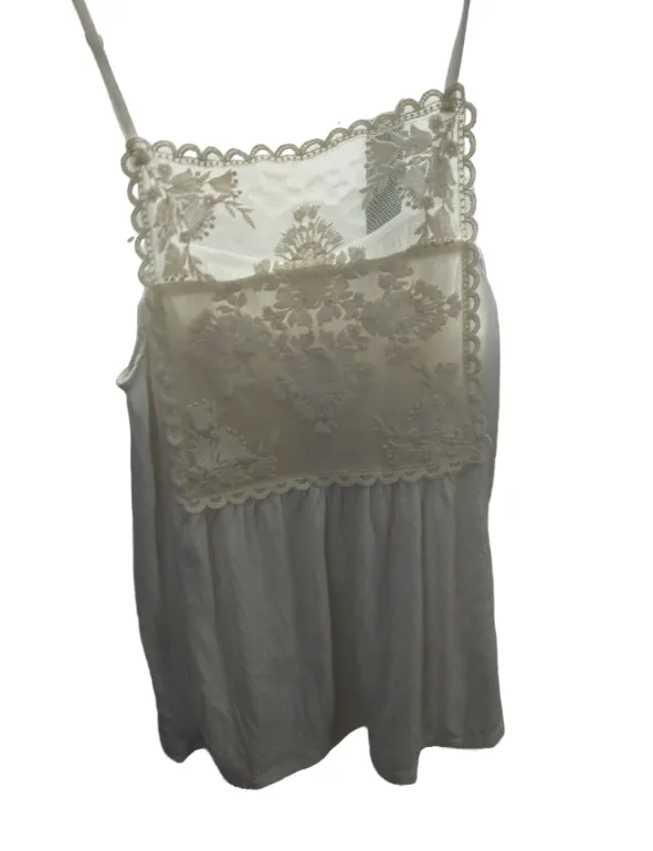 Top blanco de breteles finos con detalles de encaje floral en la parte superior. Posee un diseño delicado y romántico, ideal para combinar con faldas o shorts en días cálidos. Su estilo etéreo lo hace perfecto para ocasiones casuales o salidas.