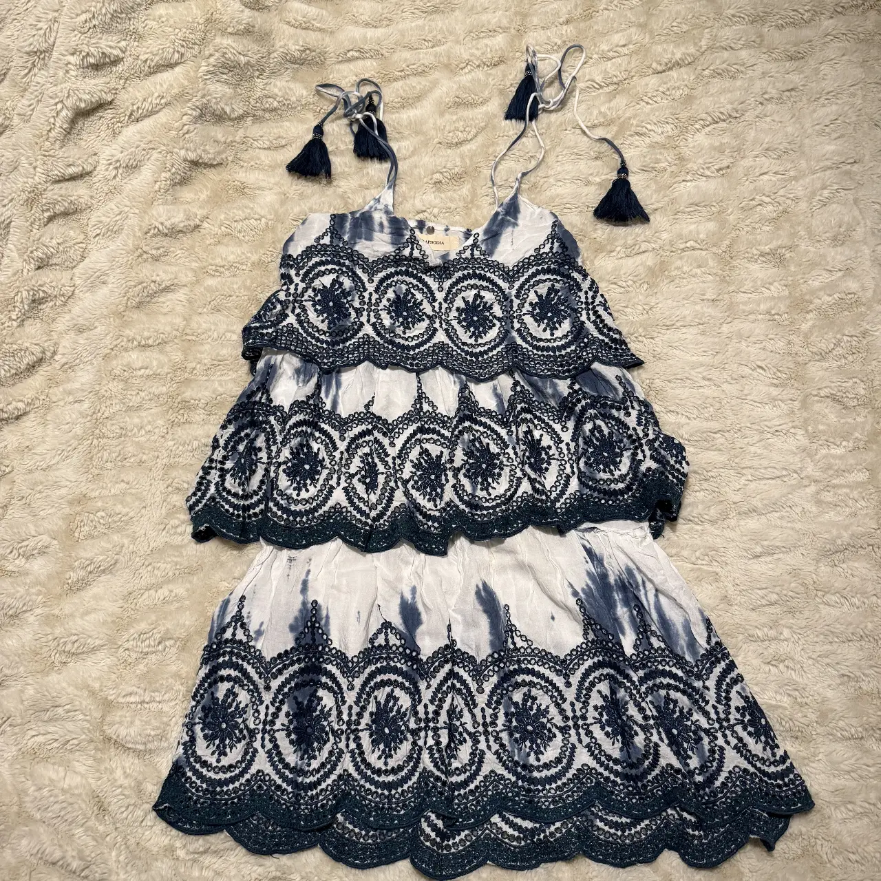Vestido corto Rapsodia de mujer con diseño tie-dye en blanco y azul. Cuenta con detalles bordados en la parte superior y en el borde inferior, con tirantes ajustables y borlas decorativas. Ideal para un look fresco y bohemio.