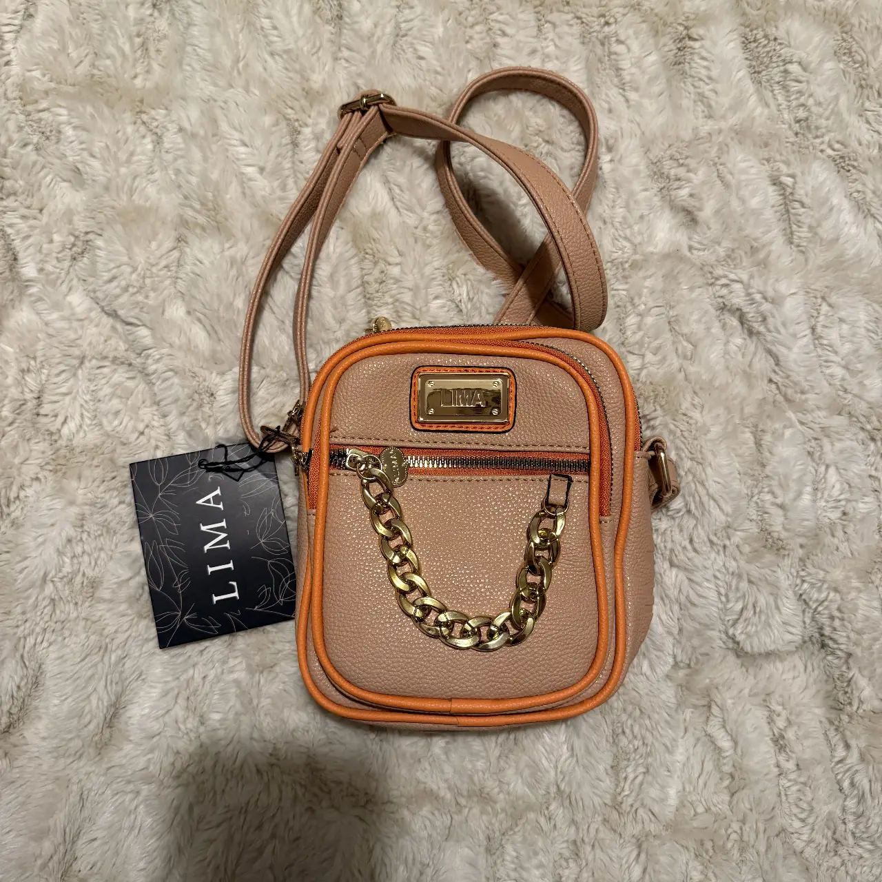 Bandolera Lima, color beige con detalles en naranja. Posee una cadena dorada como adorno y una correa ajustable. Ideal para llevar lo esencial con estilo.