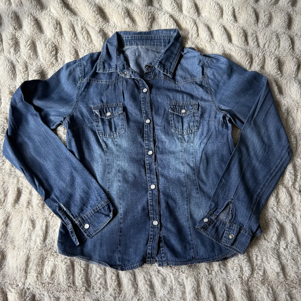 Camisa de jean azul, con dos bolsillos delanteros y botones. Ideal para un look casual y versátil.