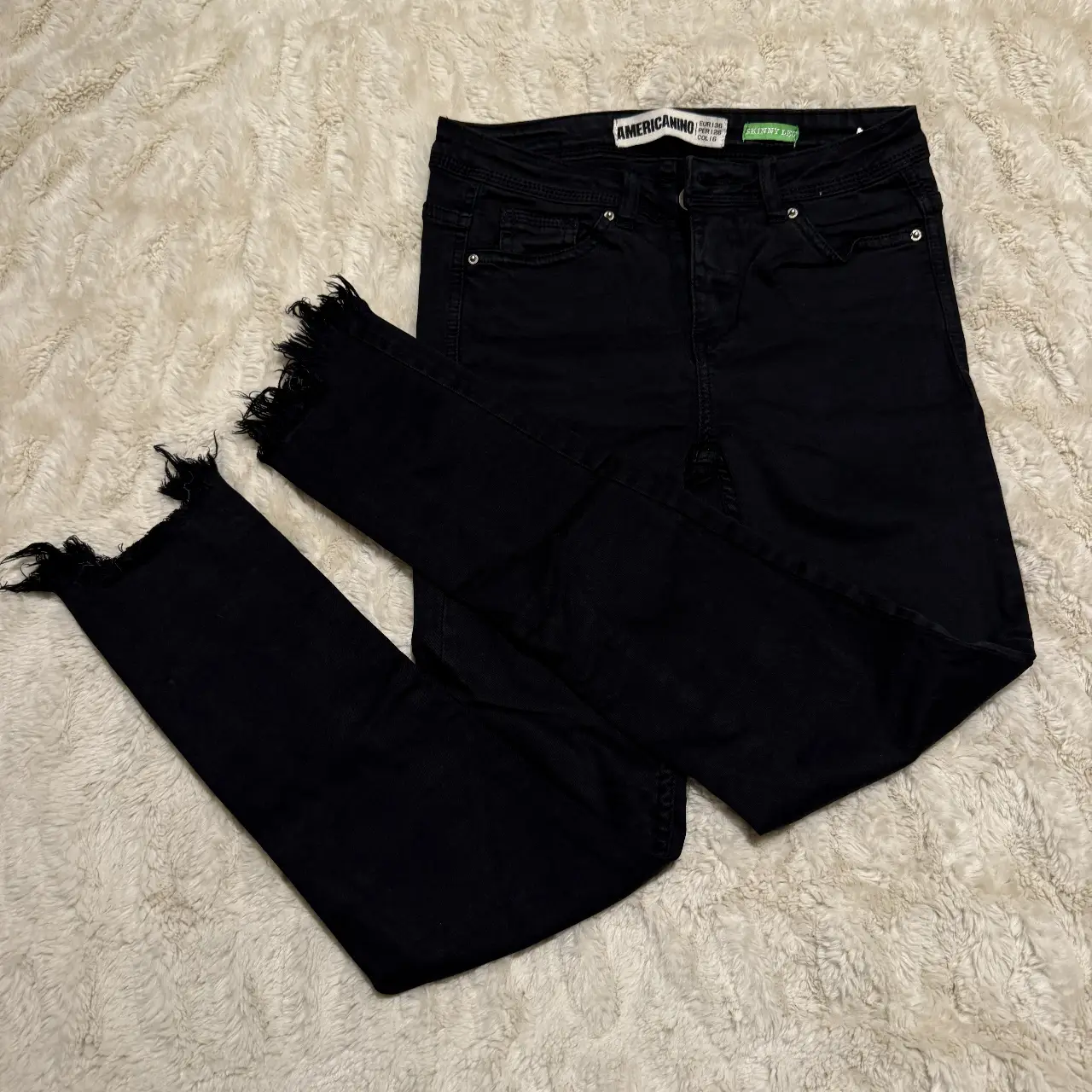 Jeans negro de tiro alto, modelo skinny con detalles de roturas y flecos en el bajo. Marca Americanino, talle 26.
