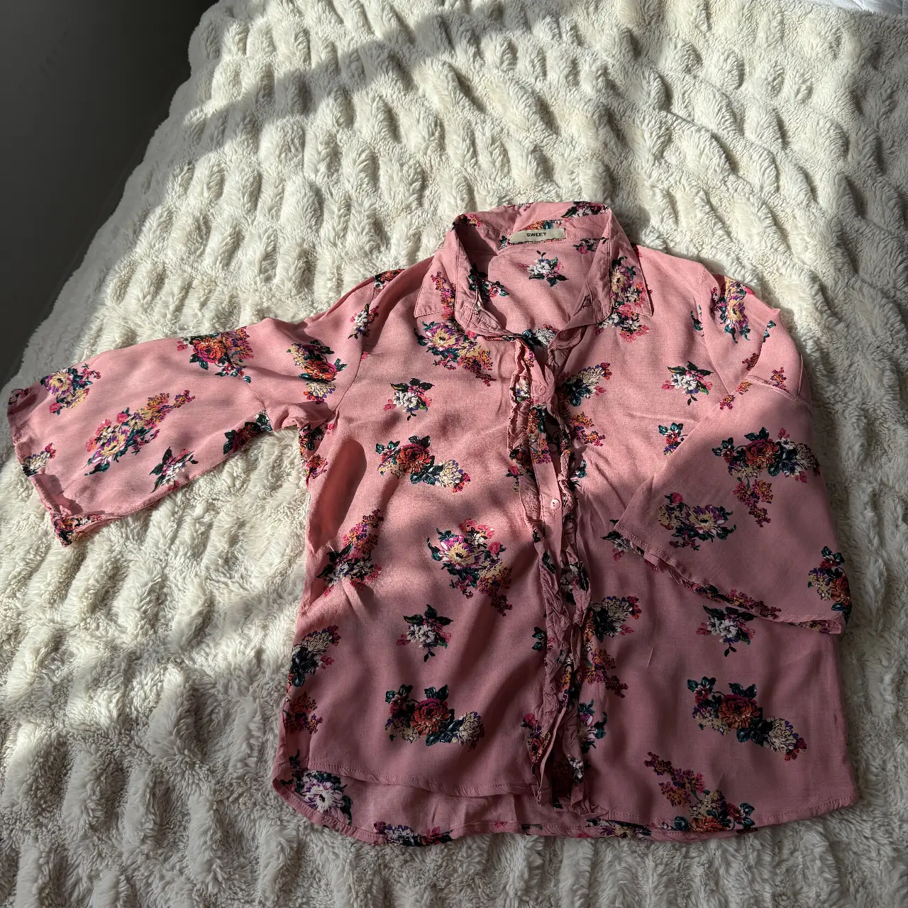 Blusa rosa SWEET con estampado floral, ideal para un look casual y femenino. Confeccionada en tela ligera y cómoda, perfecta para la primavera/verano. Detalles de volantes y botones.