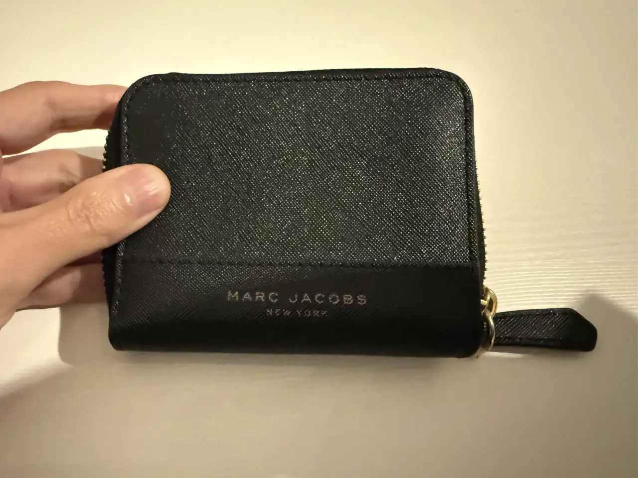 Billetera negra de cuero con cierre y logo de Marc Jacobs. Ideal para llevar tarjetas, billetes y monedas. Diseño compacto y elegante.
